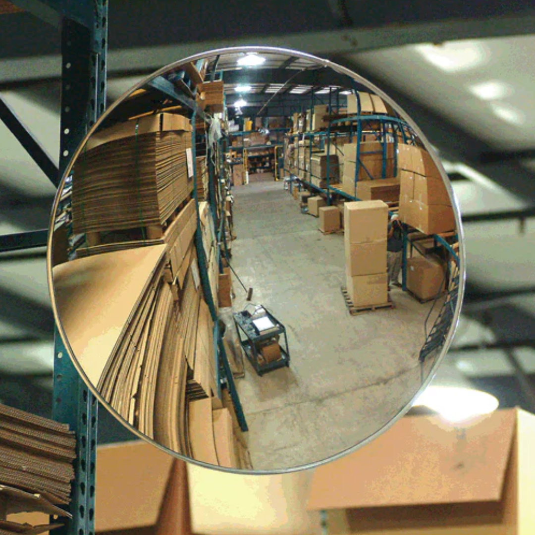 Industrial convex safety mirror in a warehouse aisle, reflecting high stacks of cardboard boxes and shelves, used for blind spot visibility, forklift safety, and workplace accident prevention in commercial storage facilities.